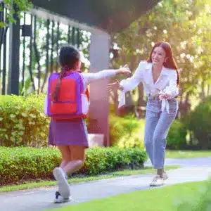A young girl joyfully runs to her co-parent after school during a custody exchange