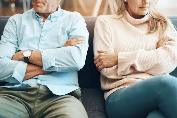 A man and woman sit apart on a couch with crossed arms, symbolizing collaborative divorce vs traditional divorce tension