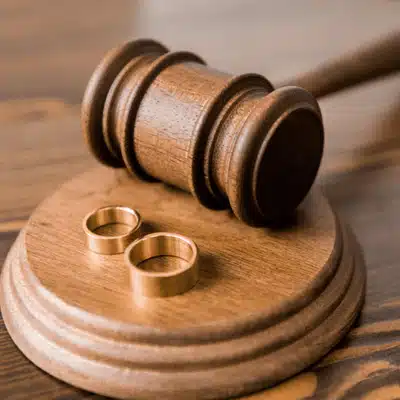 Wooden gavel and two wedding rings on a block represent collaborative divorce vs traditional divorce legal implications