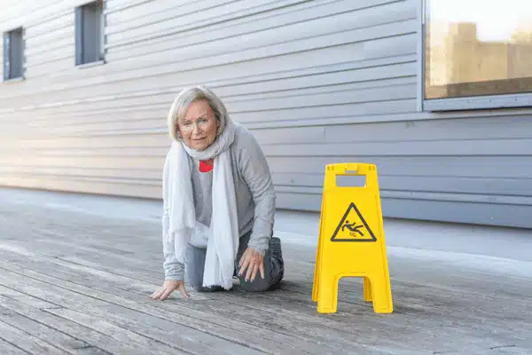 An elderly woman kneels after slipping near a caution sign on a wooden deck