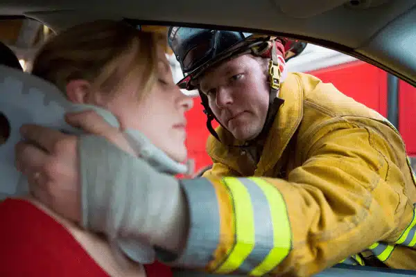 A firefighter wearing protective gear fits a neck brace on a car accident victim inside a vehicle