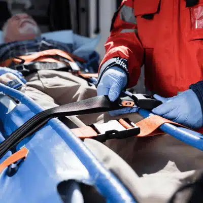 Emergency responder straps patient to stretcher, demonstrating common injuries in car accidents requiring immobilization