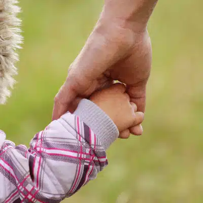 Closeup adult holds child's hand outdoors, illustrating physical custody meaning as daily caregiving and residence