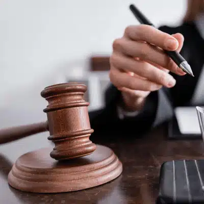 Judge's hand holds pen near gavel on desk, representing courtroom decisions and legal proceedings authority