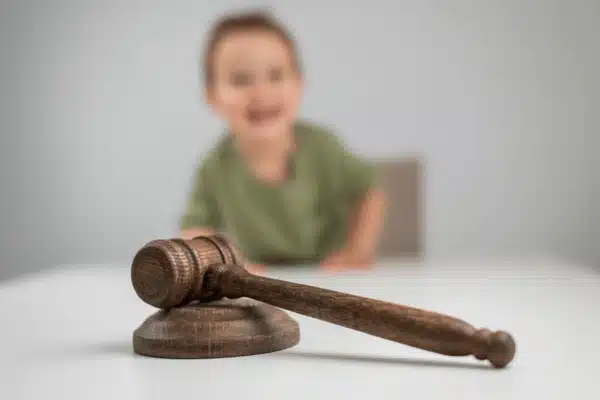Wooden judge's gavel on desk, child blurred behind, symbolizing family court custody proceedings and decisions