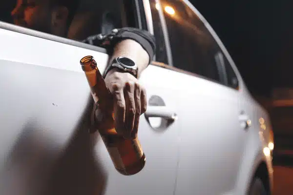Hand holds beer bottle outside car window at night, illustrating impaired driving risk scenario danger