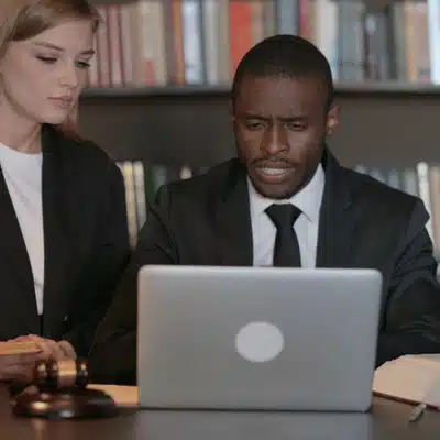 Defense attorneys review case video on laptop in law library, preparing DUI defense strategy arguments