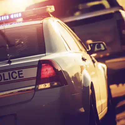 Police cruiser with lights approaches vehicle during roadside stop, documenting potential DUI investigation at sunset